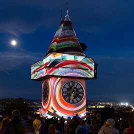 Graz Clock Tower at night with colorful Klanglicht projection and city view