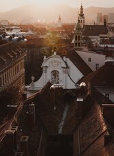 Blick über die Dächer und Kirchtürme der Grazer Altstadt im warmen Abendlicht, mit dem Plabutsch im Hintergrund