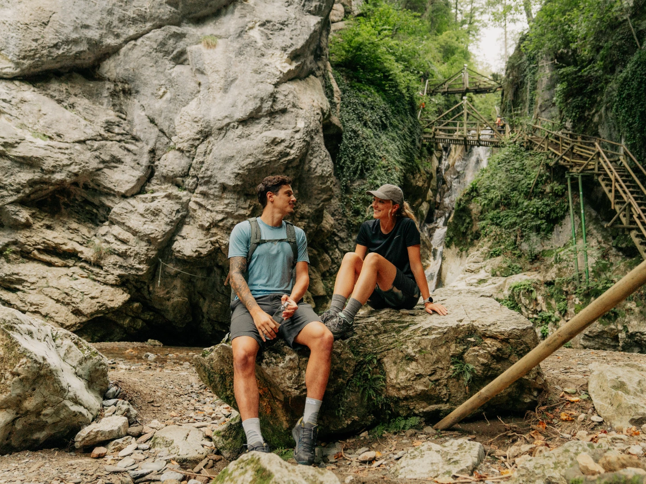 Zwei Wanderer sitzen auf Felsen vor hölzernen Stegen in der Kesselfallklamm