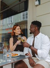 Two guests toast with white wine while enjoying regional cuisine at a dining venue in Graz.