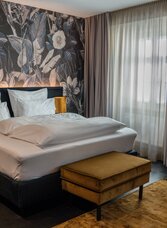 Modernes Doppelzimmer im Aiola Living Graz mit floral gestalteter Wand und großen Fenstern