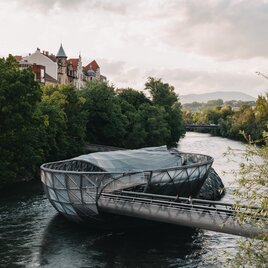 Moderne Murinsel in Graz bei leicht bewölktem Himmel und grünem Flussufer