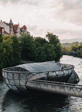 Moderne Murinsel in Graz bei leicht bewölktem Himmel und grünem Flussufer