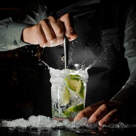 Cocktail mit Limetten wird vom Barkeeper wild umgerührt