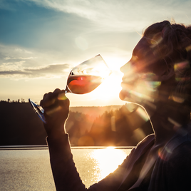 Frau trinkt ein Glas Schilcher vor einer wunderbaren Sonnenuntergangskulisse am Stausee Soboth