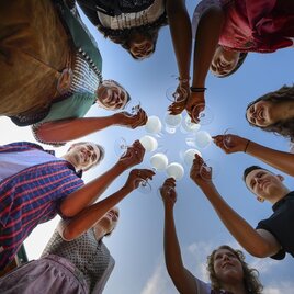 Gruppe in trachtigen Gewand stößt mit Wein an - von unten fotografiert. 