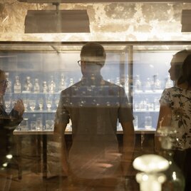 Zwei Besucher mit einem Guide im Burgmuseum Archeo Norico stehen vor einer Glasvitrine