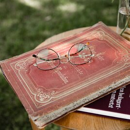 Buch mit rotem historischen Einband auf der eine runde goldene Lesebrille liegt.