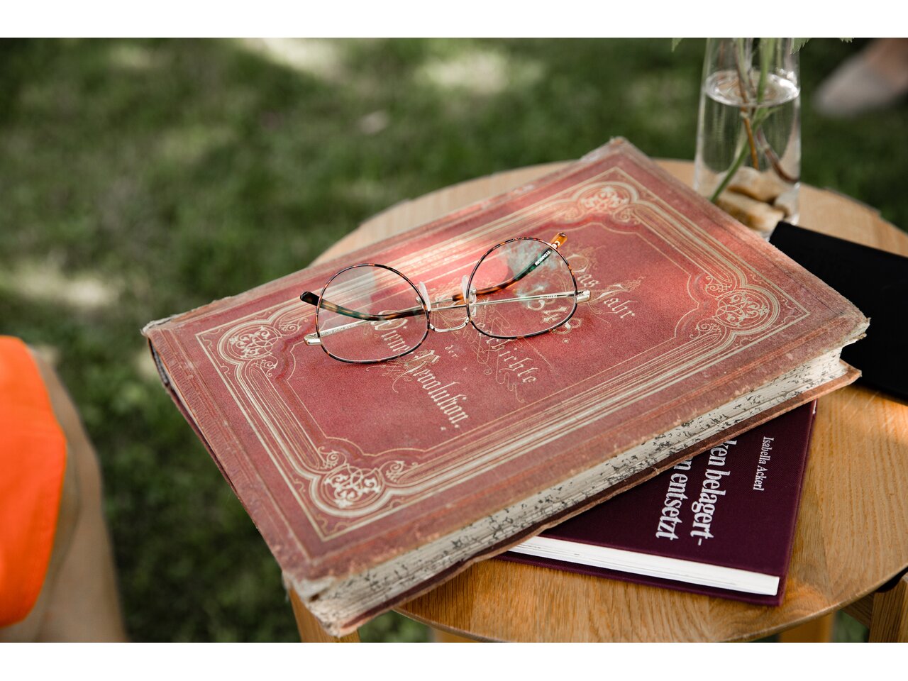 Buch mit rotem historischen Einband auf der eine runde goldene Lesebrille liegt.