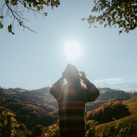 Frau steht in einem Weingarten und blickt in die Sonne | © Lukas Elsnegg