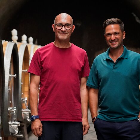 Weinbauer Hannes Harkamp (links) und Heimatleuchten Moderator Richard Deutinger (rechts) posieren für ein Foto im Weinkeller des Weinguts Harkamp | © Servus TV | Lena Moik