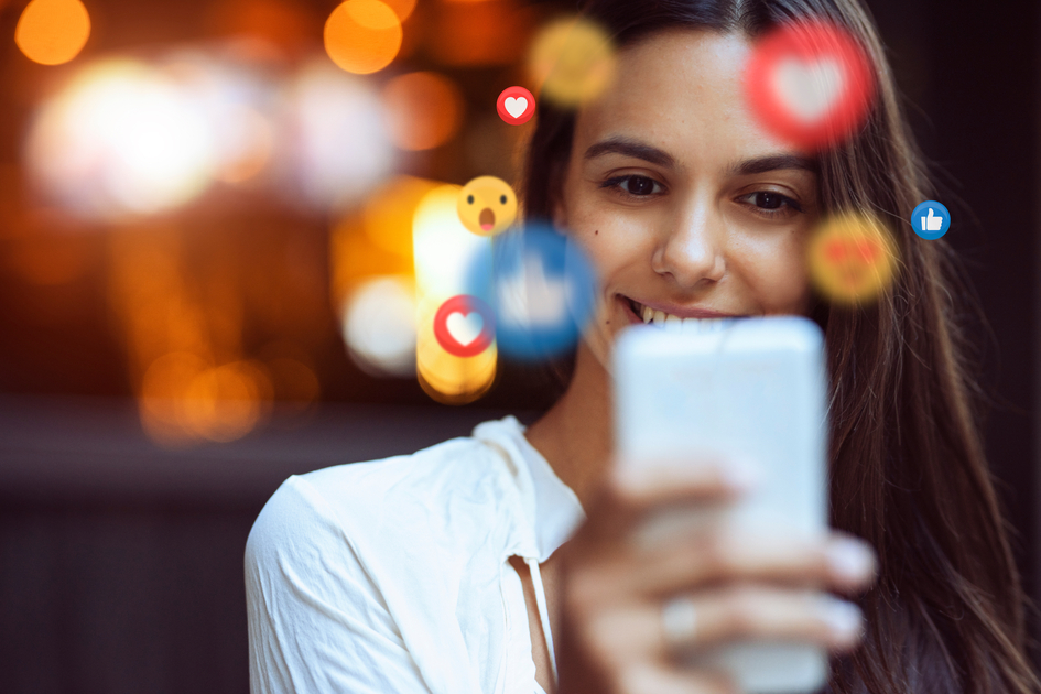 A beautiful young woman blogger, vlogger or influencer is receiving emoji and emoticon reactions in her mobile smart phone device while making a post, sharing or video logging on social media | © 2015 Parpoulas Thomas Andreas | Thomas Andreas Parpoulas
