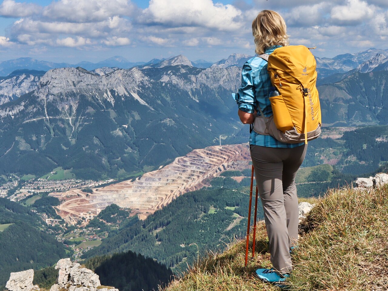 Frau blickt auf den Erzberg hinab vom Stadelstein Gipfelkreuz umgeben von hohen Bergen.