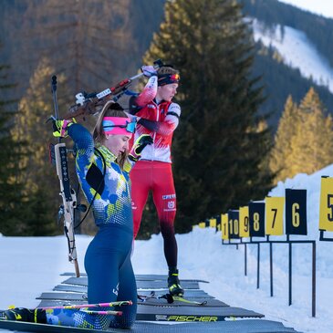 2 Sportlerinnen eine steht und eine kniet beim Schießstand im Schnee.