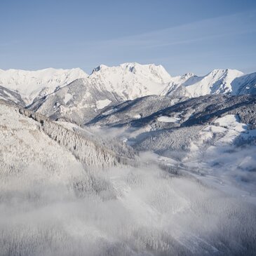 Eine winterliche Bergkulisse vor strahlend blauem Himmel mit etwas Nebel.