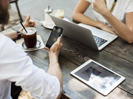 Menschen arbeiten mit Handy und Laptop an einem Tisch draußen