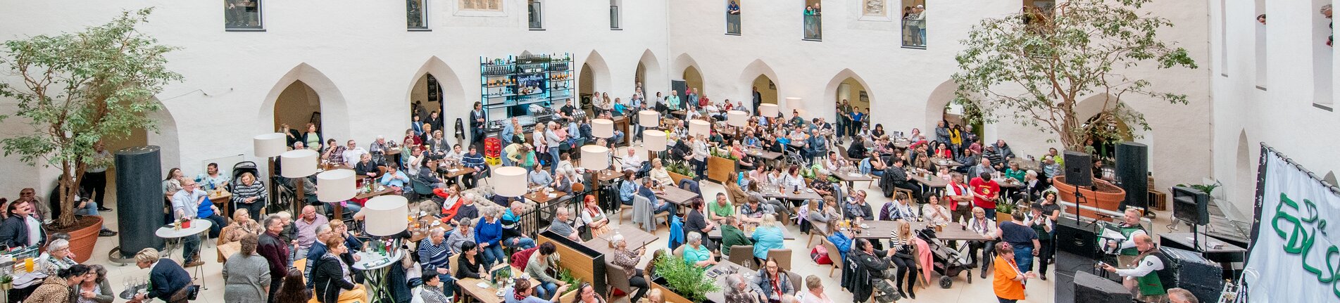 Ein überdachter Innenhof mit aufgebauter Bühne und voll besetzten Publikumstischen.