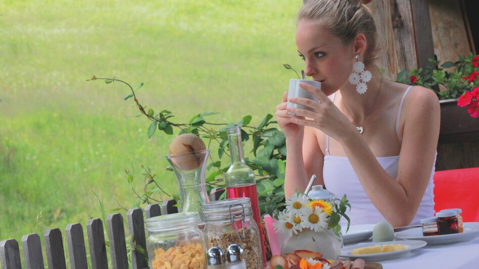 Frau trinkt aus Tasse während sie beim Frühstück sitzt und in die Natur schaut