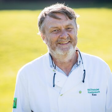 Klaus Lobnik in Kochmontur vor einer grünen Wiese im Sonnenschein.