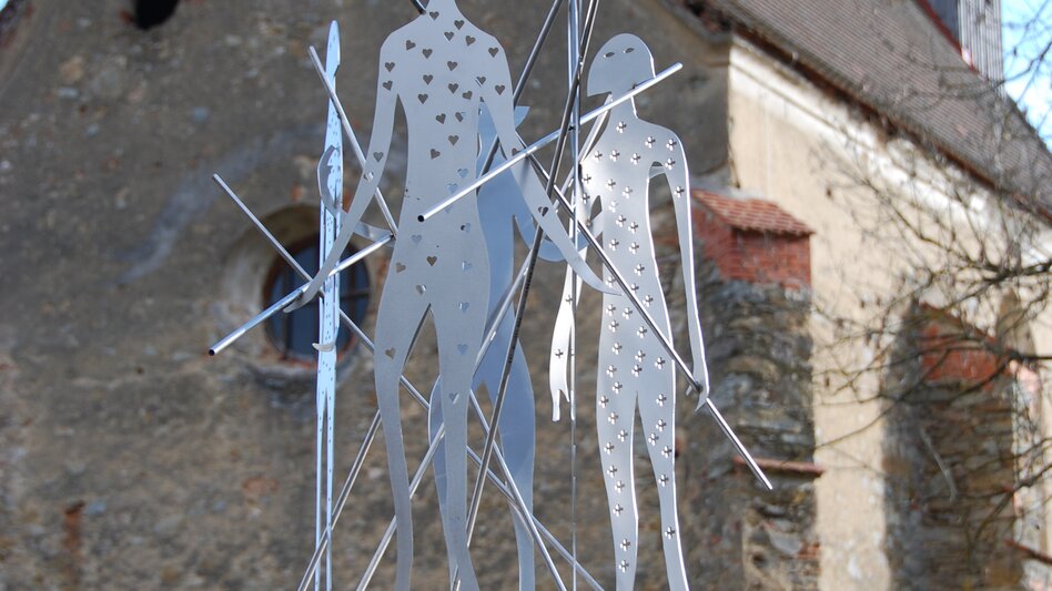 Eine Skulptur aus Eisen im Hintergrund eine Kirchenmauer