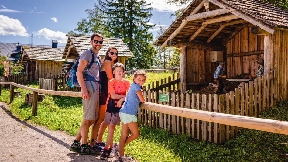 Eine Familie mit zwei kleinen Kindern, stehen vor einer Schauhütte und sehen Richtung Kamera