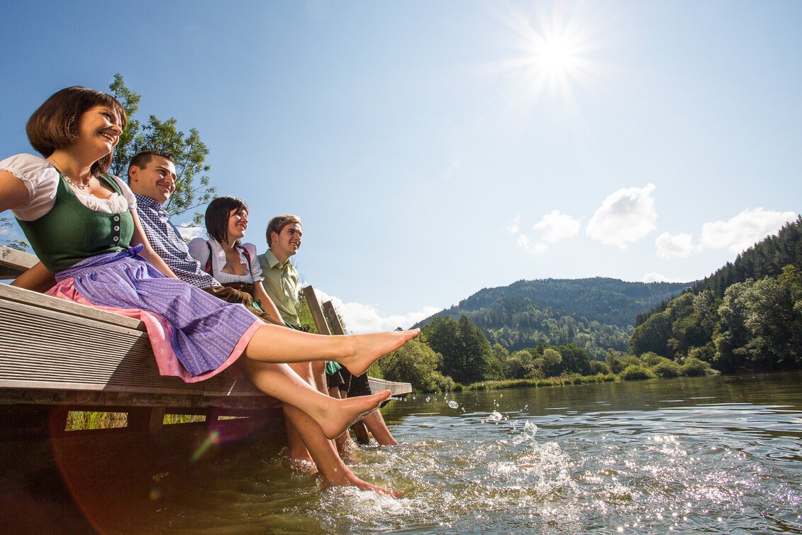 Eine Gruppe von Menschen sitzen auf einen Holzsteg mit den Füßen im Wasser