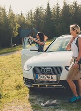 Eine SUV steht auf einer Alm, neben dem Auto drei Frauen die die Aussicht genießen