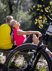 Im Vordergrund steht ein E-Bike, im Hintergrund sitzt ein Pärchn auf einer Bank mit Blick auf die Mürz