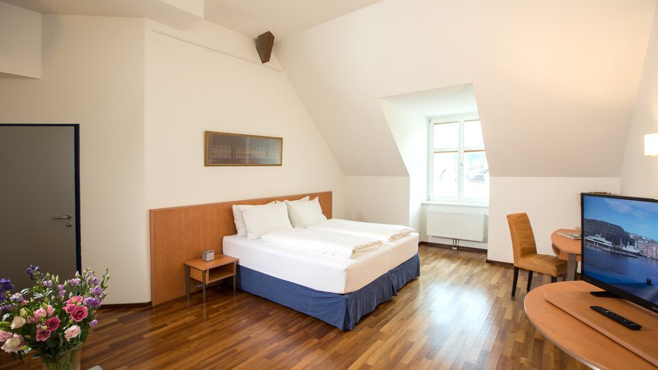 Ansicht eines Doppelzimmers im Hotel Böhlerstern mit Holzboden, Fenster, Fernseher und einem Tisch mit Sessel