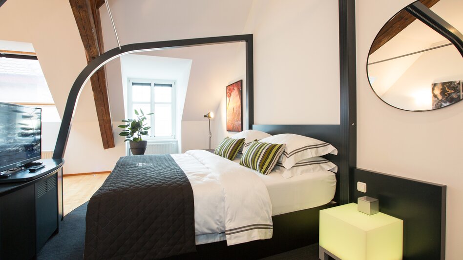 Die Suite im Hotel Böhlerstern mit Doppelbett, Fenster, Fernseher, einem Spiegel, Topfpflanze und einem Bild an der Wand