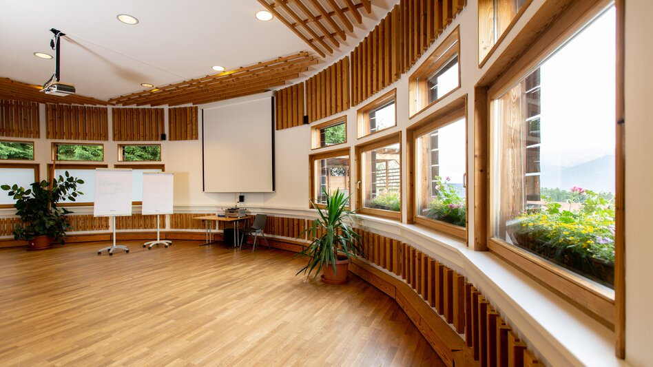 Ein lichtdurchflutet Seminarraum, mit vielen Holzelementen, grünen Pflanzen, Beamerleinwand und Flip-Charts.