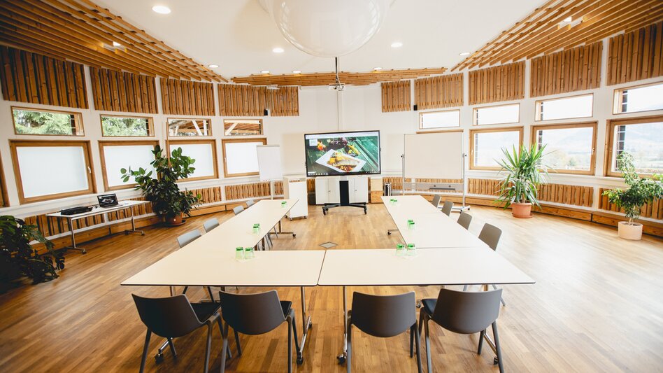 Ein lichtdurchfluteter Seminarraum, mit vielen Holzelementen, grünen Pflanzen, Beamerleinwand und Flip-Charts.