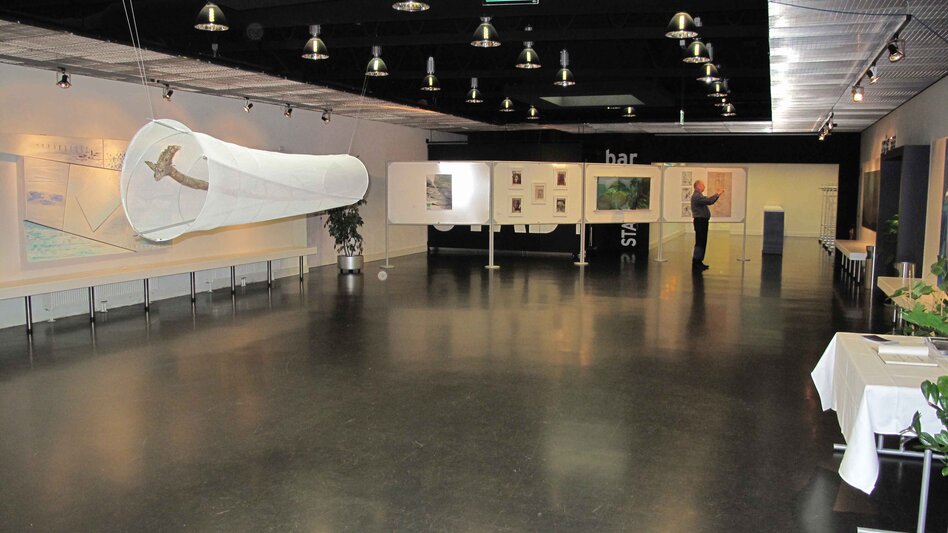 Ansicht des Foyers im Stadtsaal Mürzzuschlag mit ausgestellten Bildern und einer dunklen Decke mit vielen Hängelampen