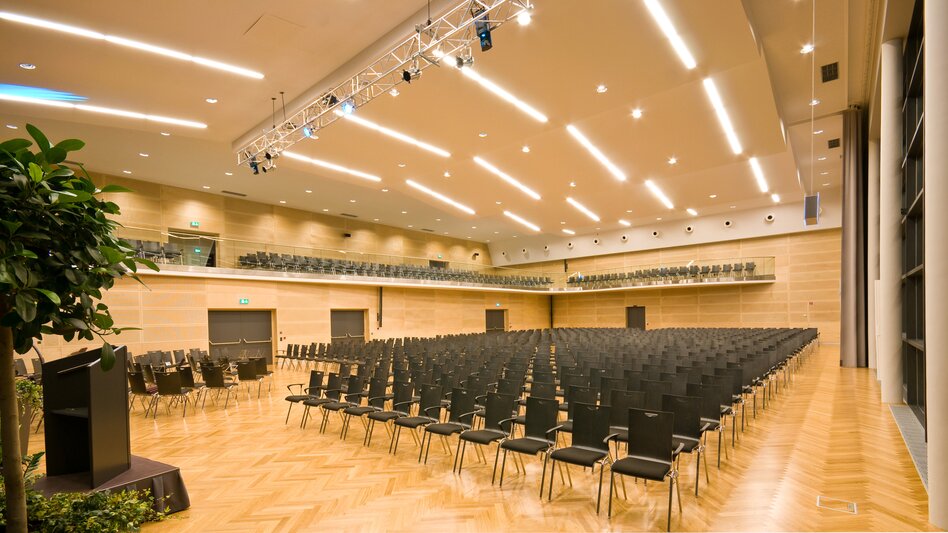 Der Große Saal mit Galerie im Veranstaltungszentrum Krieglach mit Kinobestuhlung hell erleuchtet und mit Pflanzen als Dekoration neben dem Bühnenbereich