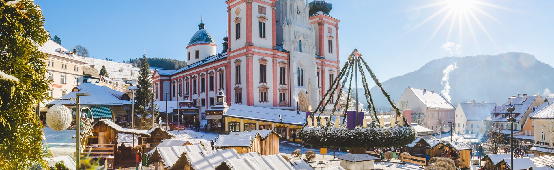 Mariazeller Basilika umgeben von geschmückten Ausstellerholzhütten mit verschneiten Dächern und dem großen Adventkranz