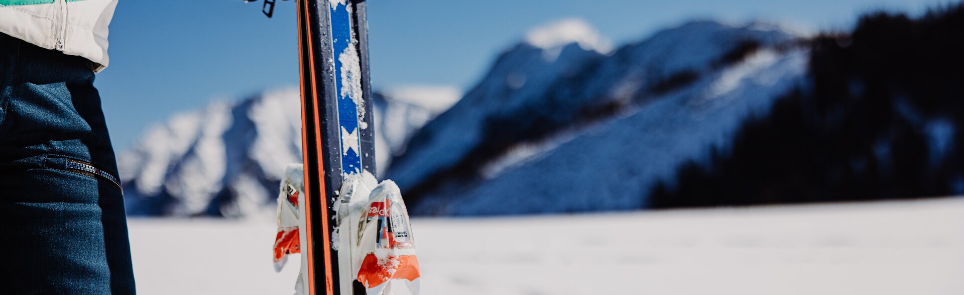 Eine Frau hält eine Ski in der Hand, im Hintergrund eine Berglandschaft