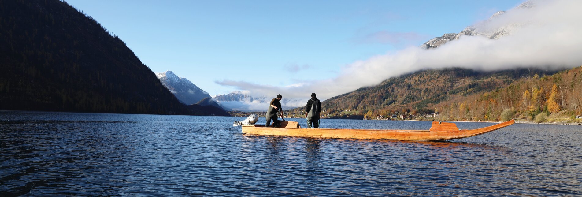 Zwei Fischer stehen auf einem kleinen Holzboot in Mitten des Sees und halten Ausschau nach Fischen. | © Fischerei Ausseerland