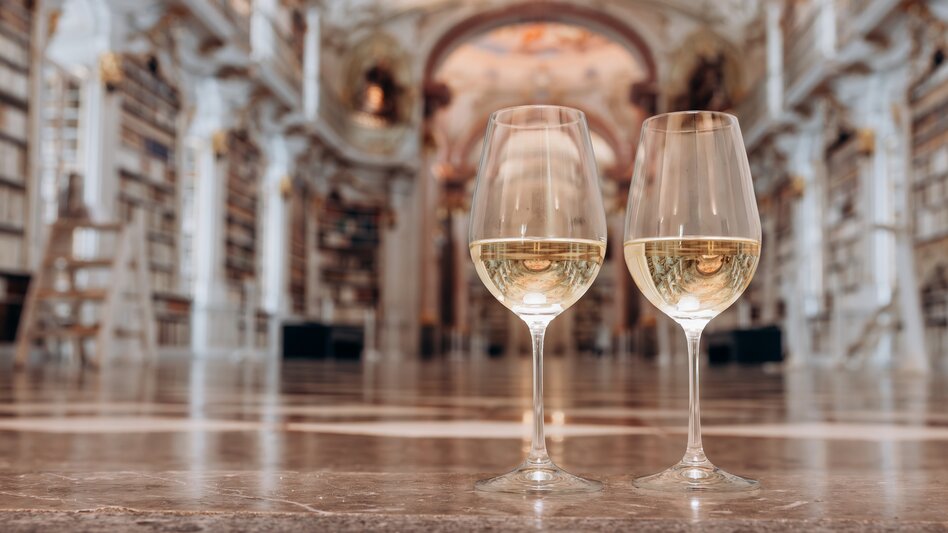 Zwei Weingläser gefüllt mit Weißwein vom Weingut Dveri Pax stehen am Boden der Stiftsbibliothek Admont