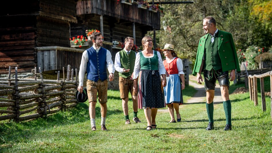 eine kleine in Tracht gekleidete Gruppe  bestehend aus drei Männern und zwei Frauen mittleren Alters spaziert durch das Österreichische Freilichtmuseum Stübing.