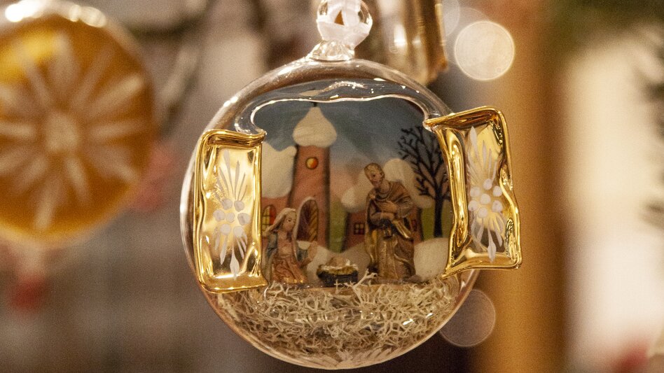 Eine handgefertigte Christbaumkugel aus Glas mit dem Motiv einer Krippe ist in Großaufnahme zu sehen.