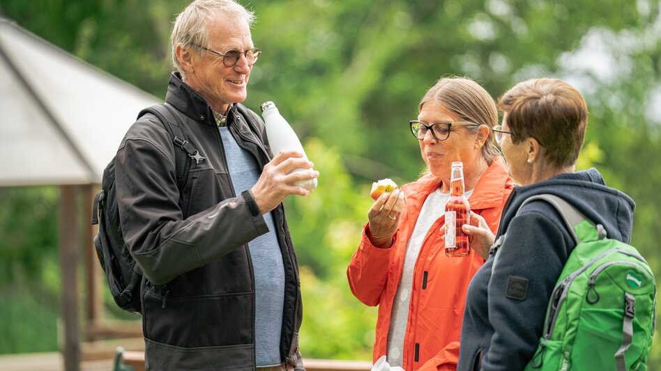 Drei Genusssportler machen eine Rast am Weg und stärken sich mit einem Apfel, Wasser und Spritzer | © STG