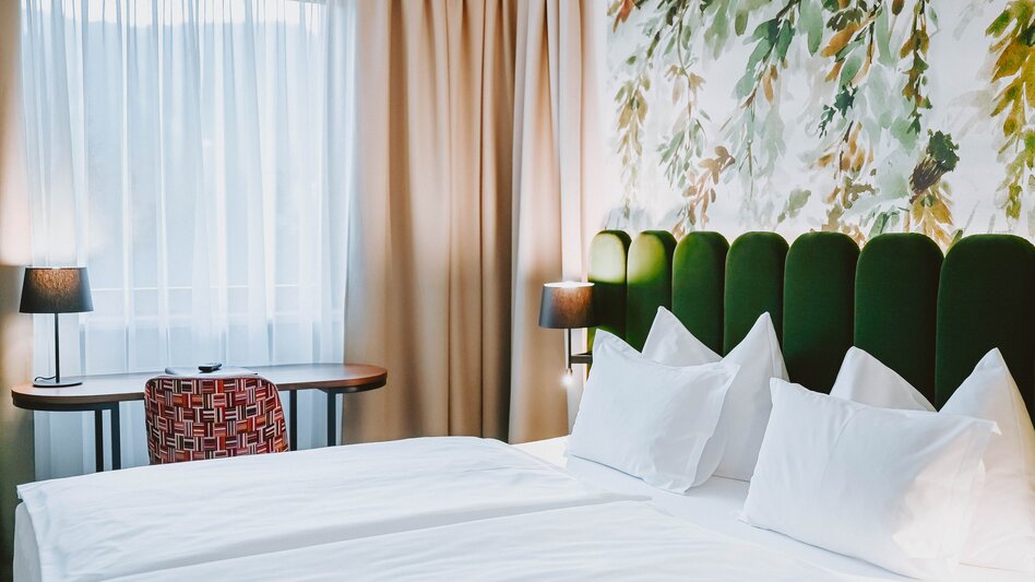 Zimmer mit Doppelbett in Naturtönen mit floraler Tapete an der grünen Bettrückseite