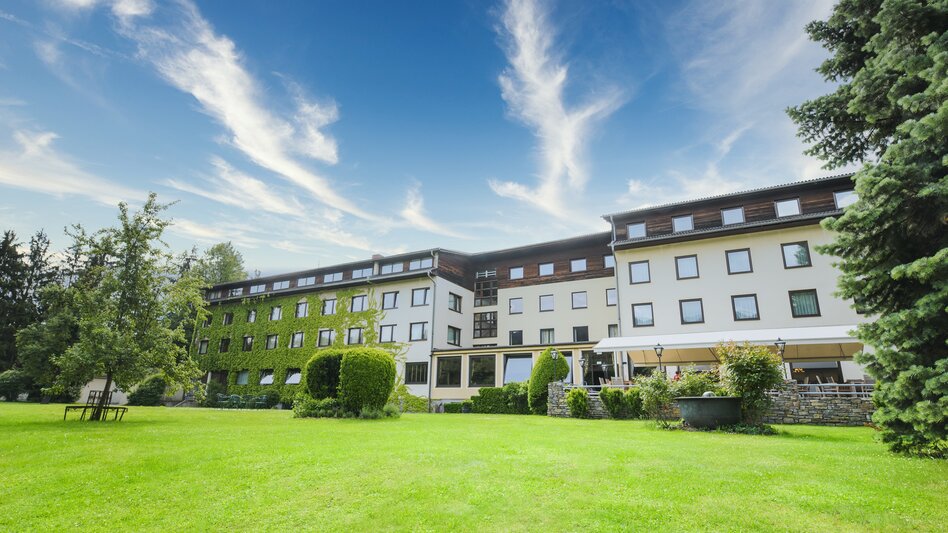 Große hoteleigene Gartenanlage mit Blick auf die beige Hotelrückseite mit ruhiger Gartenterrasse