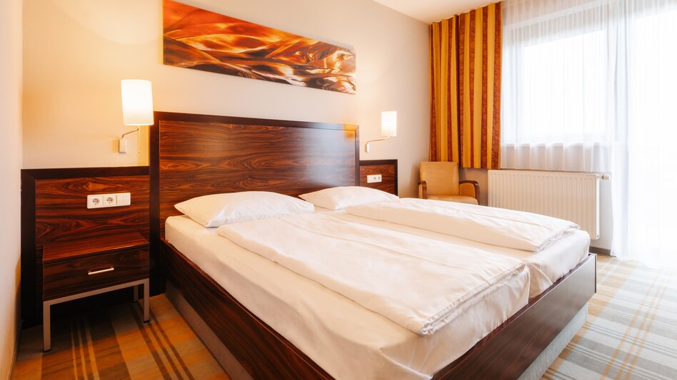 Doppelzimmer in dunklem Braun kombiniert mit orange am Teppichboden und in den Streifen der Vorhänge
