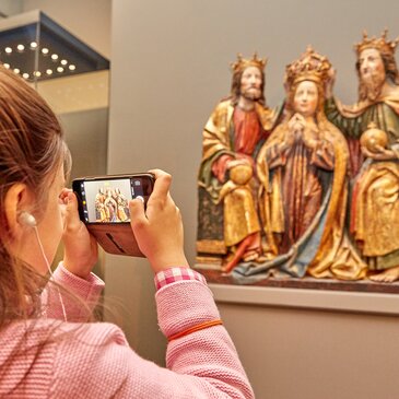 Ein Kind fotografiert mit Smartphone eine religiöse Darstellung aus der Zeit der Gotik | © Stift Admont