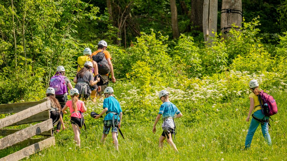 Eine Gruppe von Kindern spaziert los. Heute steht Kistenklettern am Programm. Dafür haben schon alle Helme und Ausrüstung angezogen.