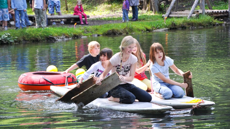 Eine Gruppe von Kindern paddelt mit einem Holz über das Wasser.