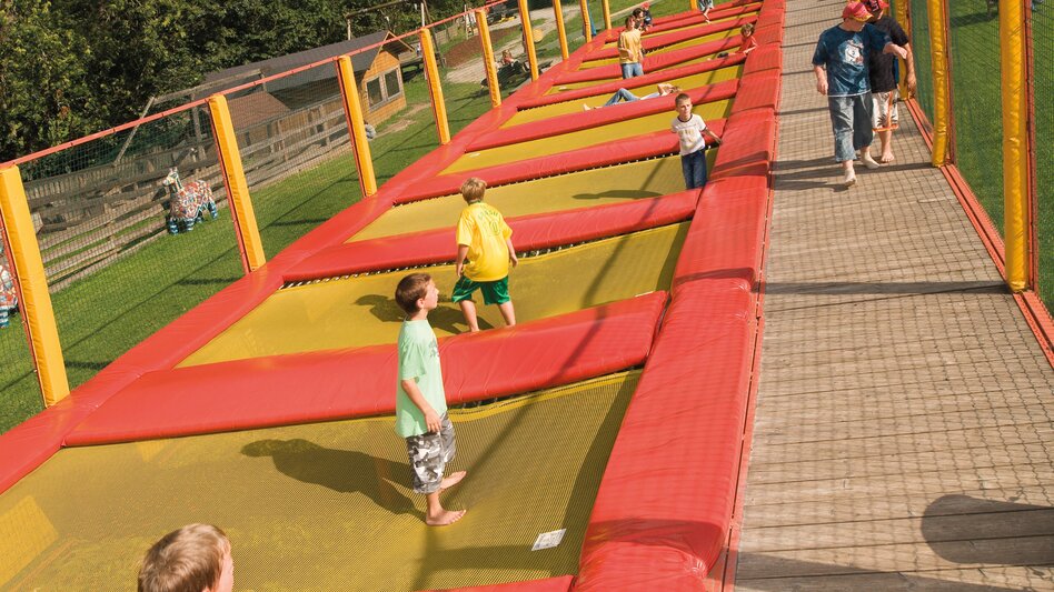 Die rot-gelbe Trampolinanlage im Freien bietet mehreren Kindern gleichzeitig die Möglichkeit sich auszutoben