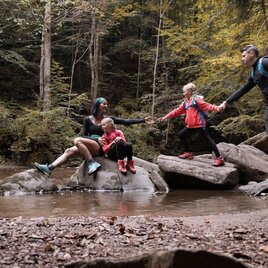 Familie auf Steinen im Bach bei einer Wanderung im Wald | © TVB Südsteiermark/Nadine Geuter
