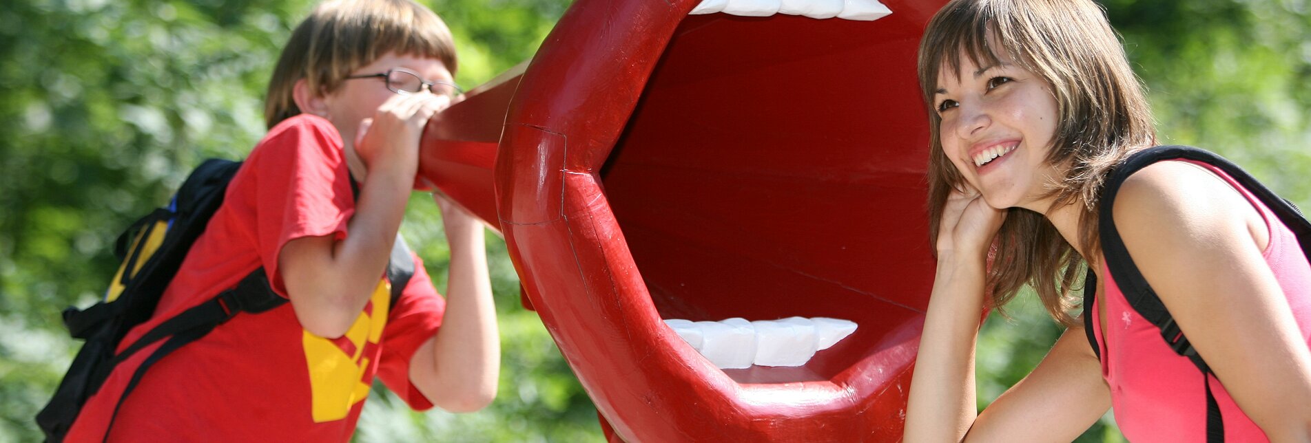 Eine Person lauschend vor einer großen Mund Skulptur | © Aldrian